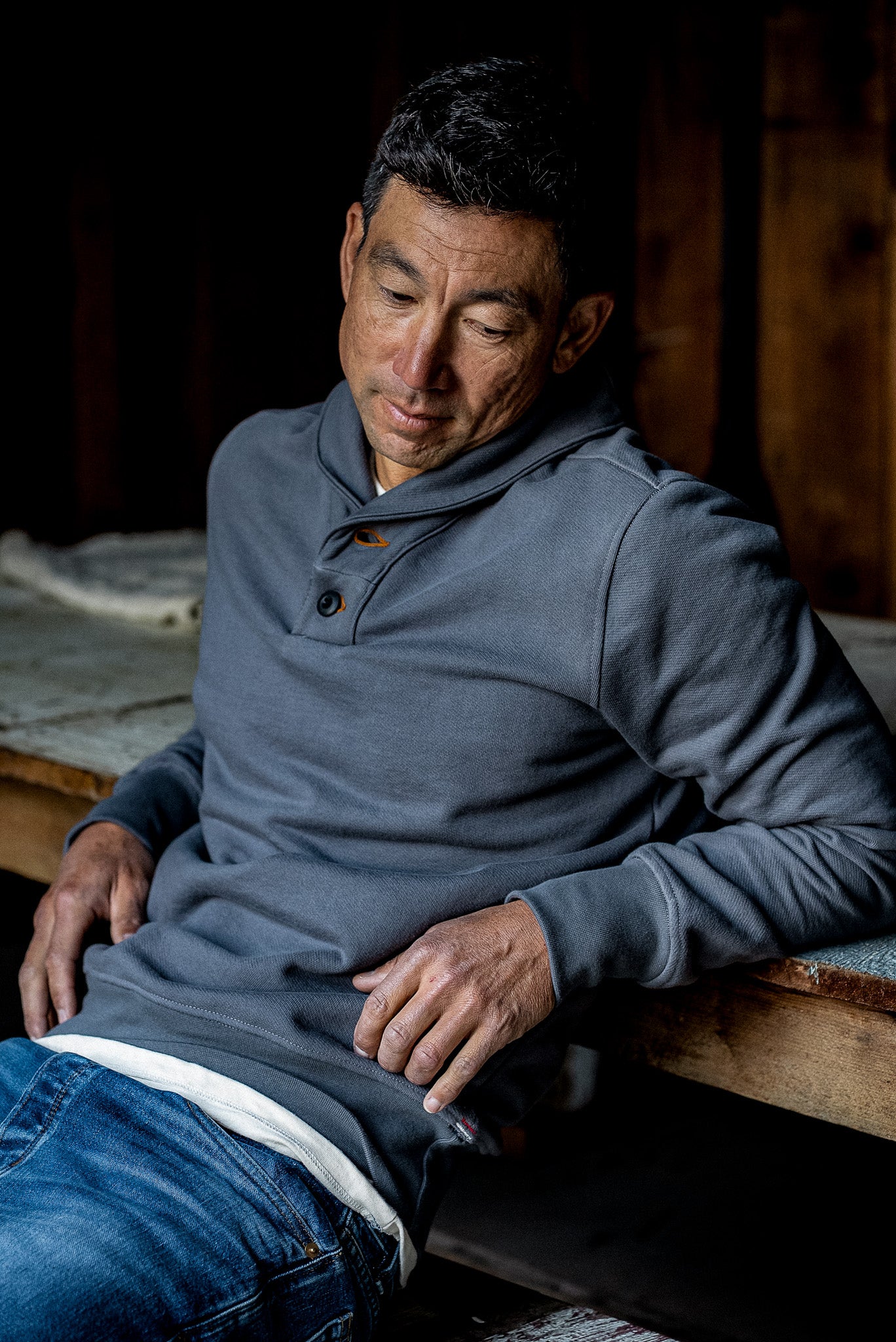 Man wearing pebble gray French terry shawl collar pullover with buttoned placket, seated.