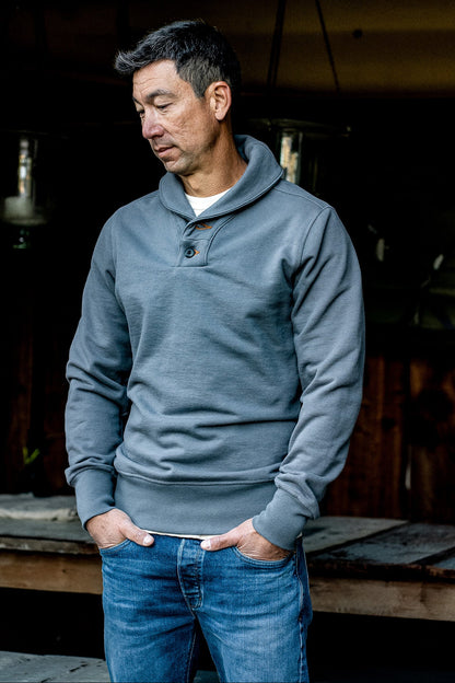 Man wearing pebble grey Bodega shawl collar French terry pullover with jeans, hands in pockets.