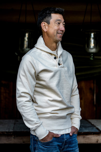 Man wearing the natural cream Bodega shawl collar pullover with button placket over blue jeans.