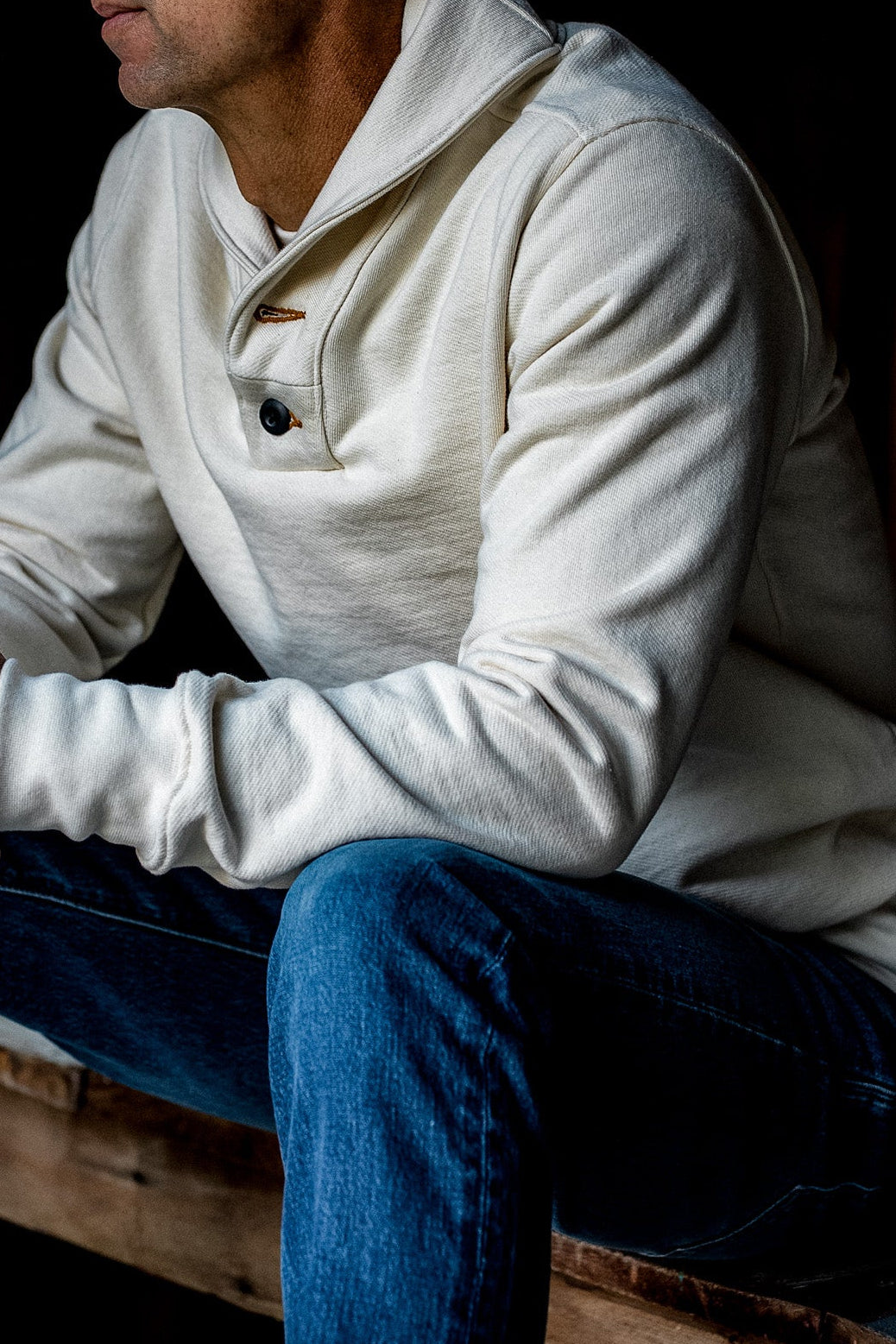 Man in a natural cream shawl collar pullover with button placket, paired with blue denim jeans.
