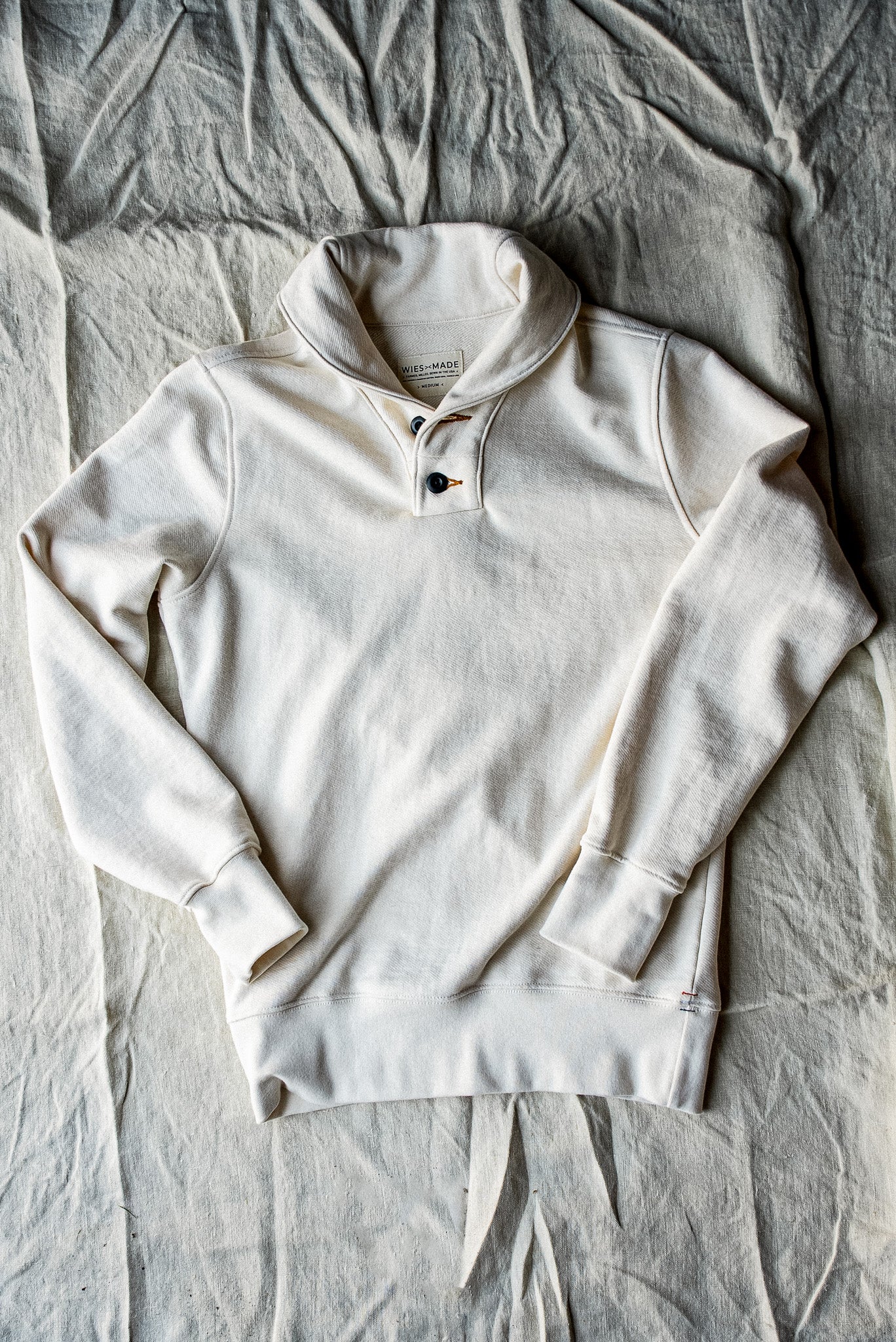 Natural cream French terry shawl collar pullover laid flat on linen, showing two-button placket.