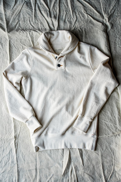 Natural cream French terry shawl collar pullover laid flat on linen, showing two-button placket.