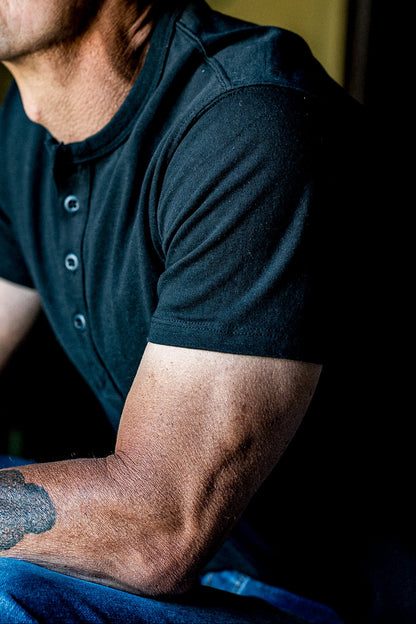Close-up of a seated man wearing the Bolinas four-button henley in dark basalt cotton.
