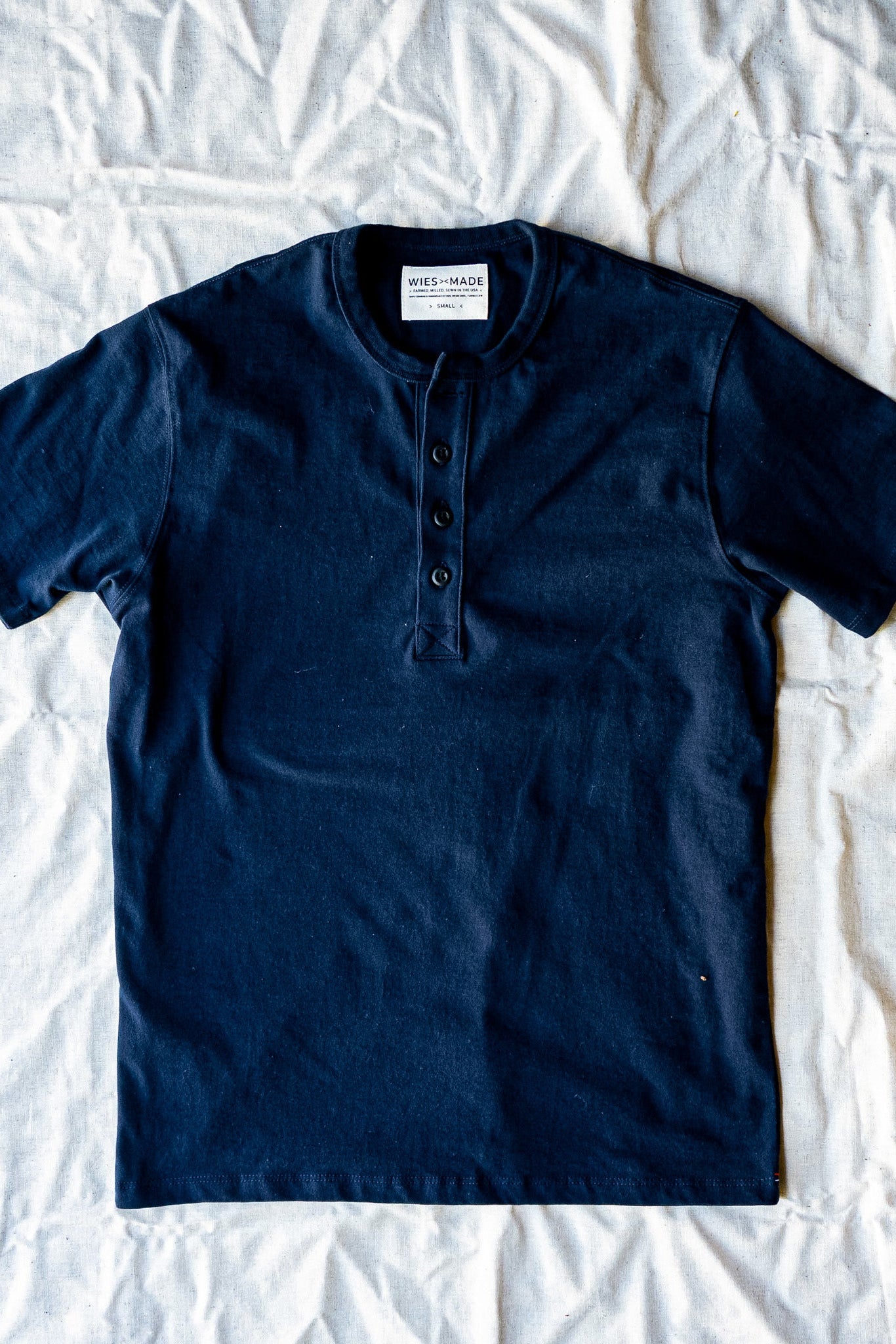 Navy short-sleeve Bolinas henley with four-button placket, laid flat on a linen sheet.