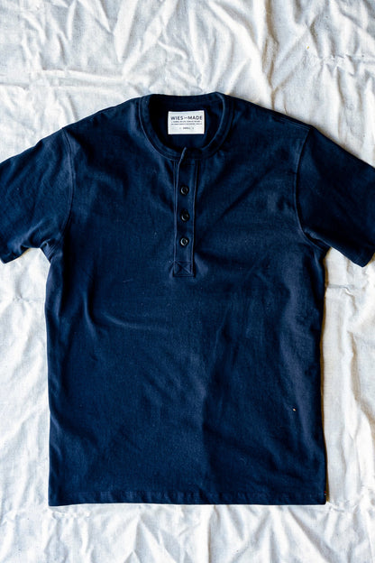 Navy short-sleeve Bolinas henley with four-button placket, laid flat on a linen sheet.