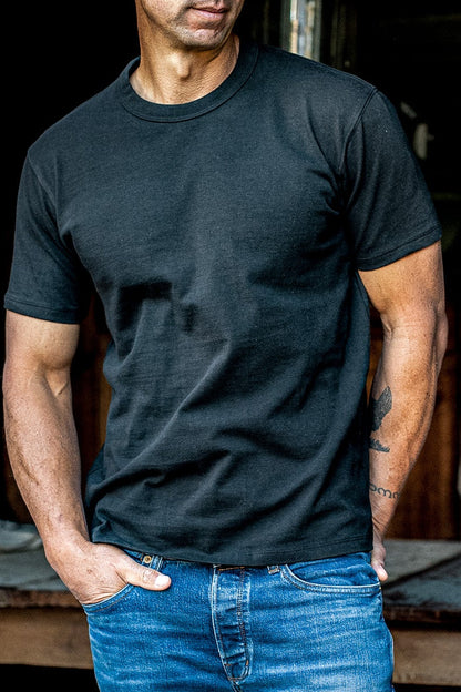 Man wearing a basalt black heavyweight crewneck tee tucked into blue jeans, hand in pocket.
