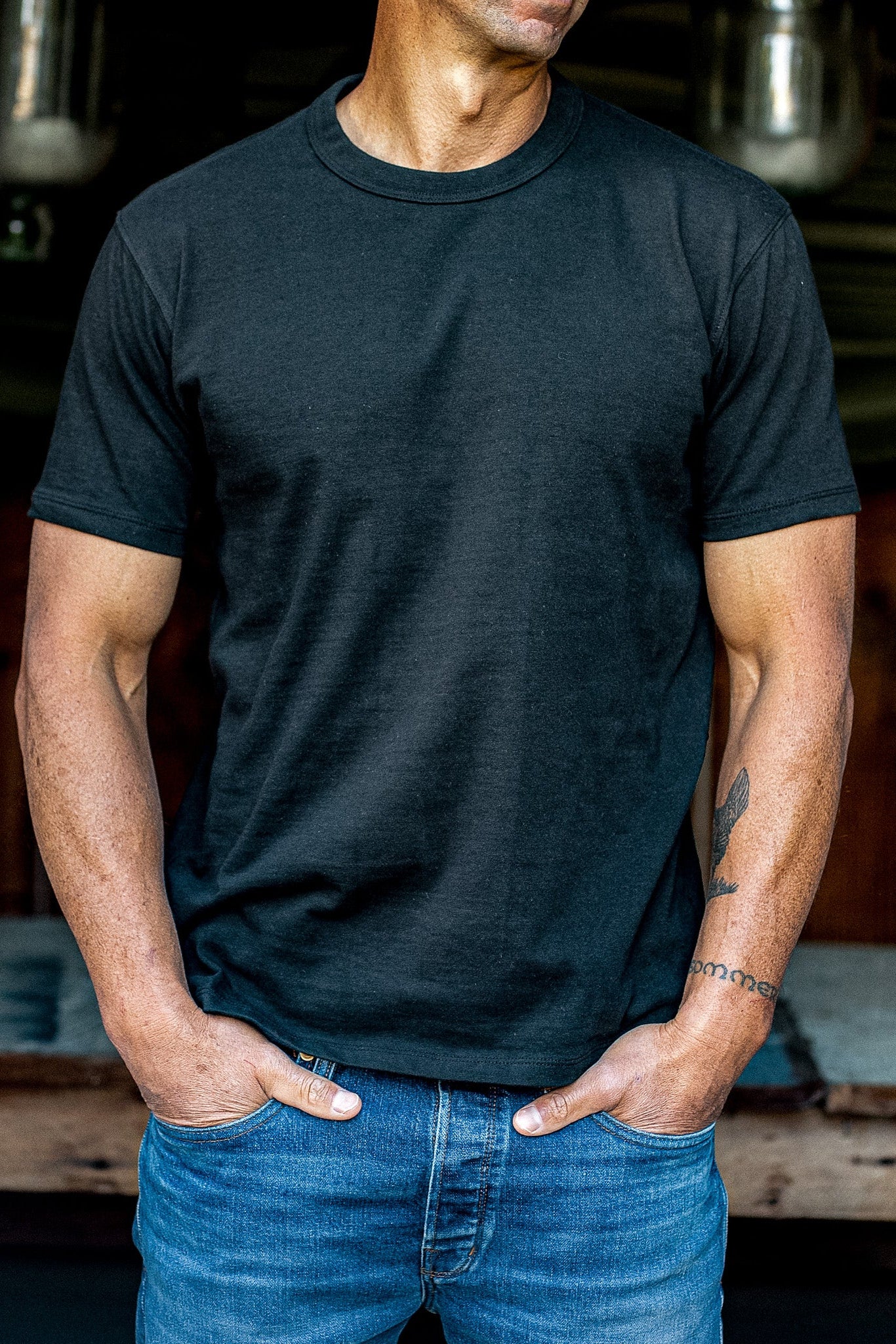 Man wearing a basalt black heavyweight cotton Bolinas tee with blue jeans, hands in pockets.