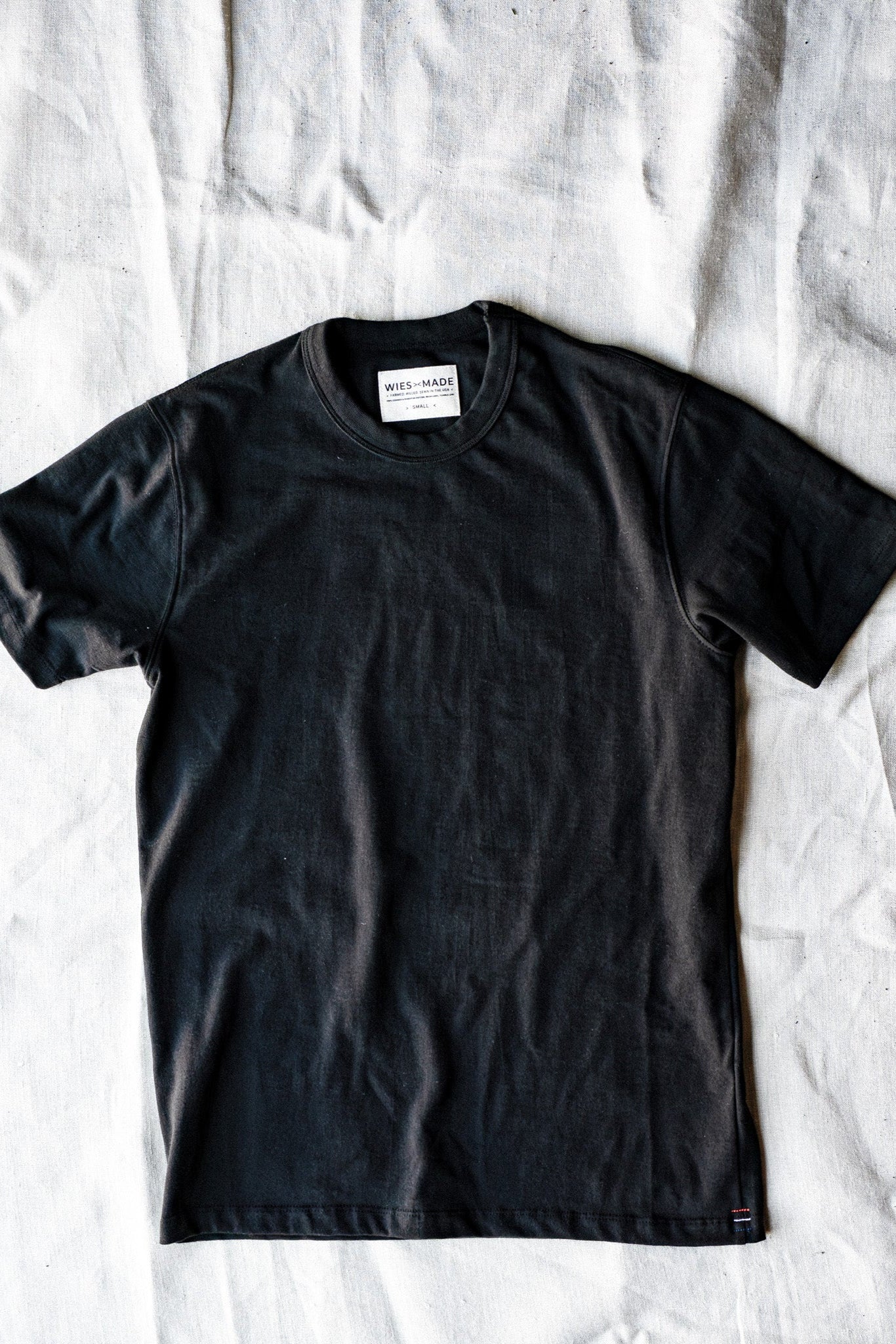 Basalt black heavyweight cotton crewneck tee laid flat on a natural linen backdrop.
