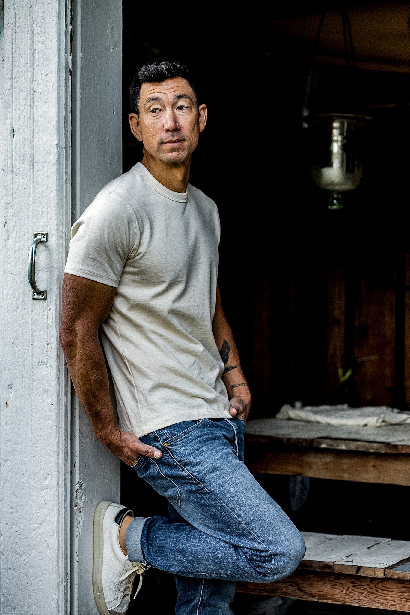 Man in a natural cotton Bolinas heavyweight tee and blue jeans leaning in a weathered doorway.
