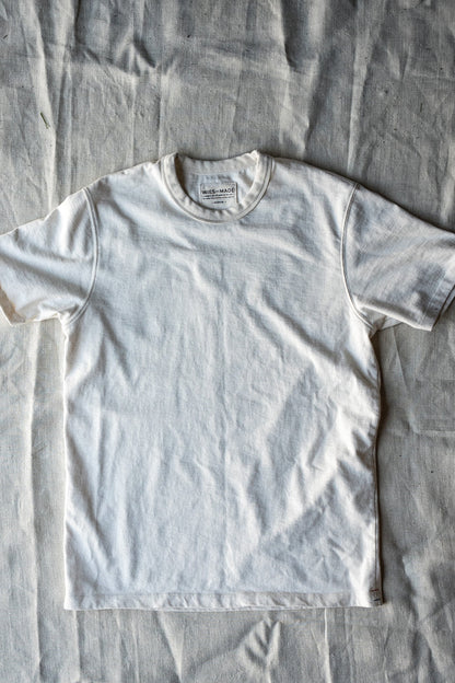 Natural white heavyweight cotton crewneck tee laid flat on a linen cloth, showing the WiesMade neck label.