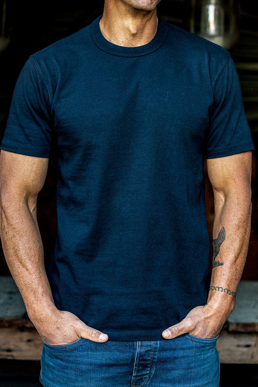 Man wearing a navy heavyweight cotton Bolinas tee with blue jeans, hands tucked into pockets.