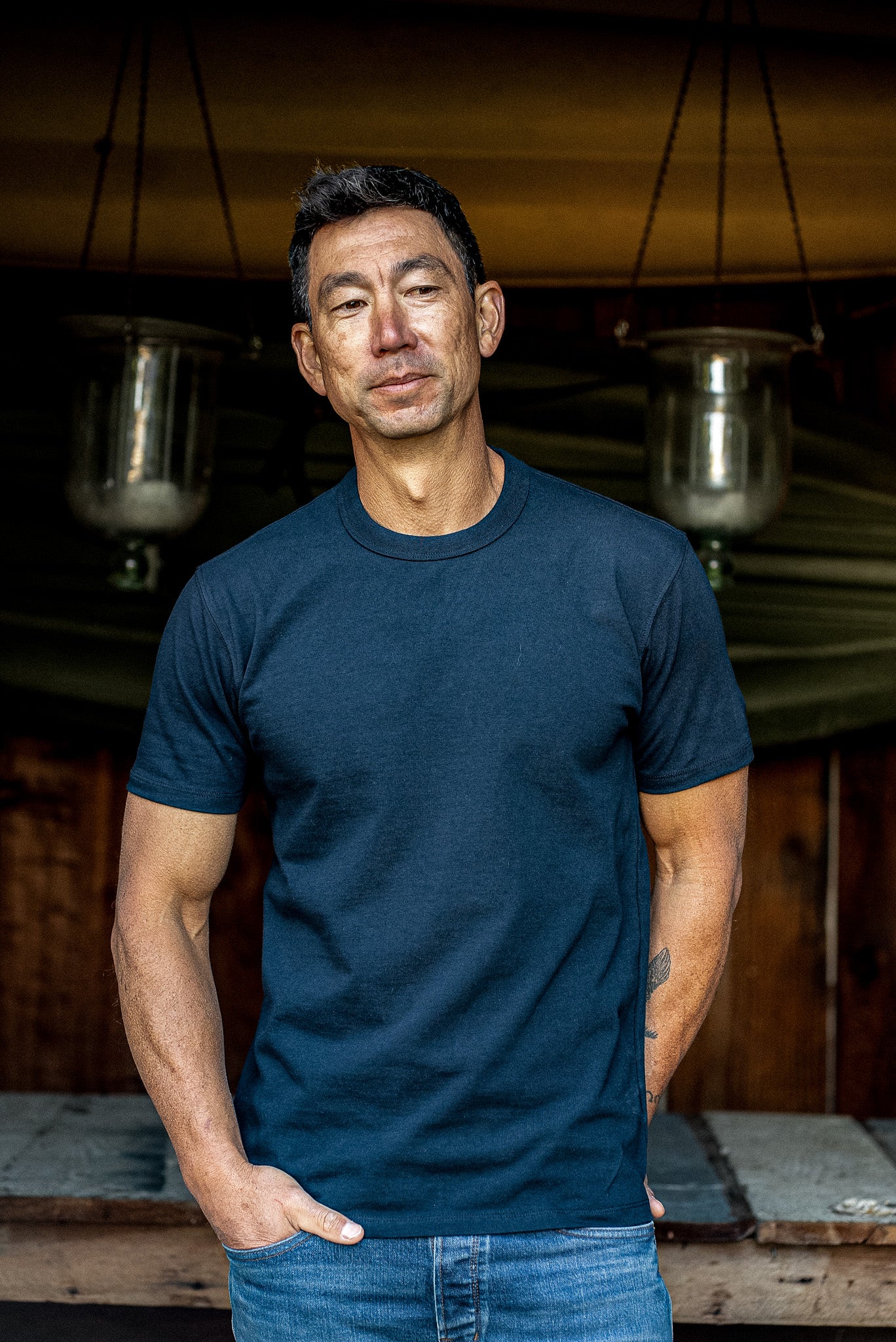 Man wearing a navy heavyweight cotton Bolinas crewneck tee with blue jeans in a rustic workshop.