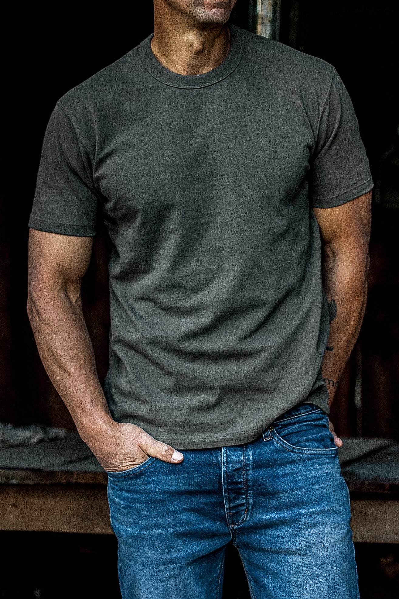 Man wearing an olive heavyweight cotton Bolinas tee tucked loosely into blue jeans.
