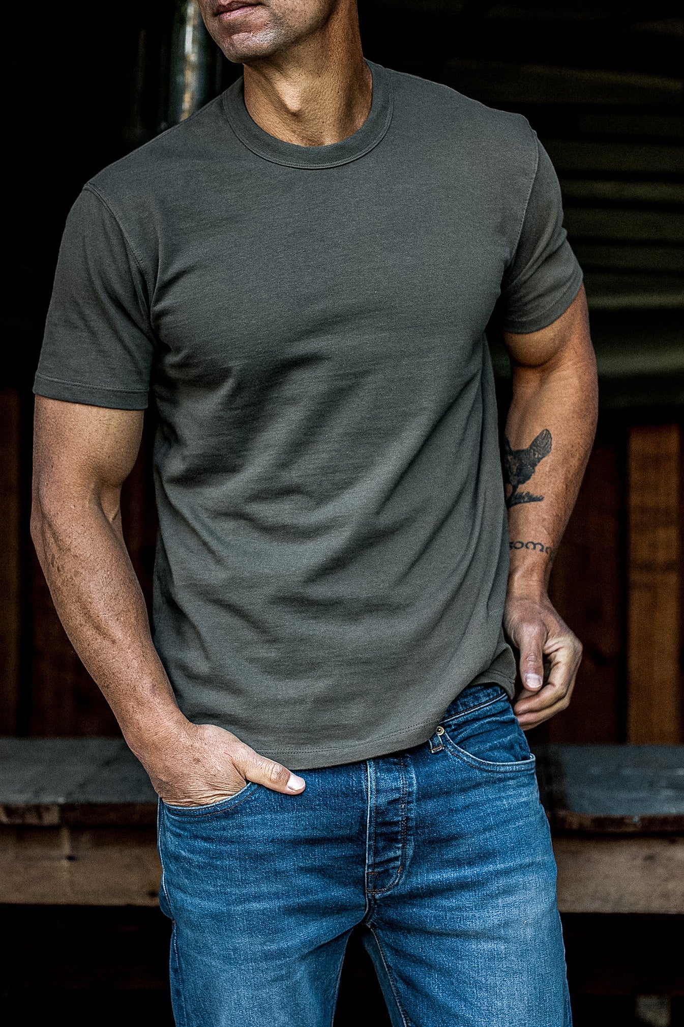 Man wearing an olive heavyweight cotton crewneck tee tucked loosely into blue jeans.