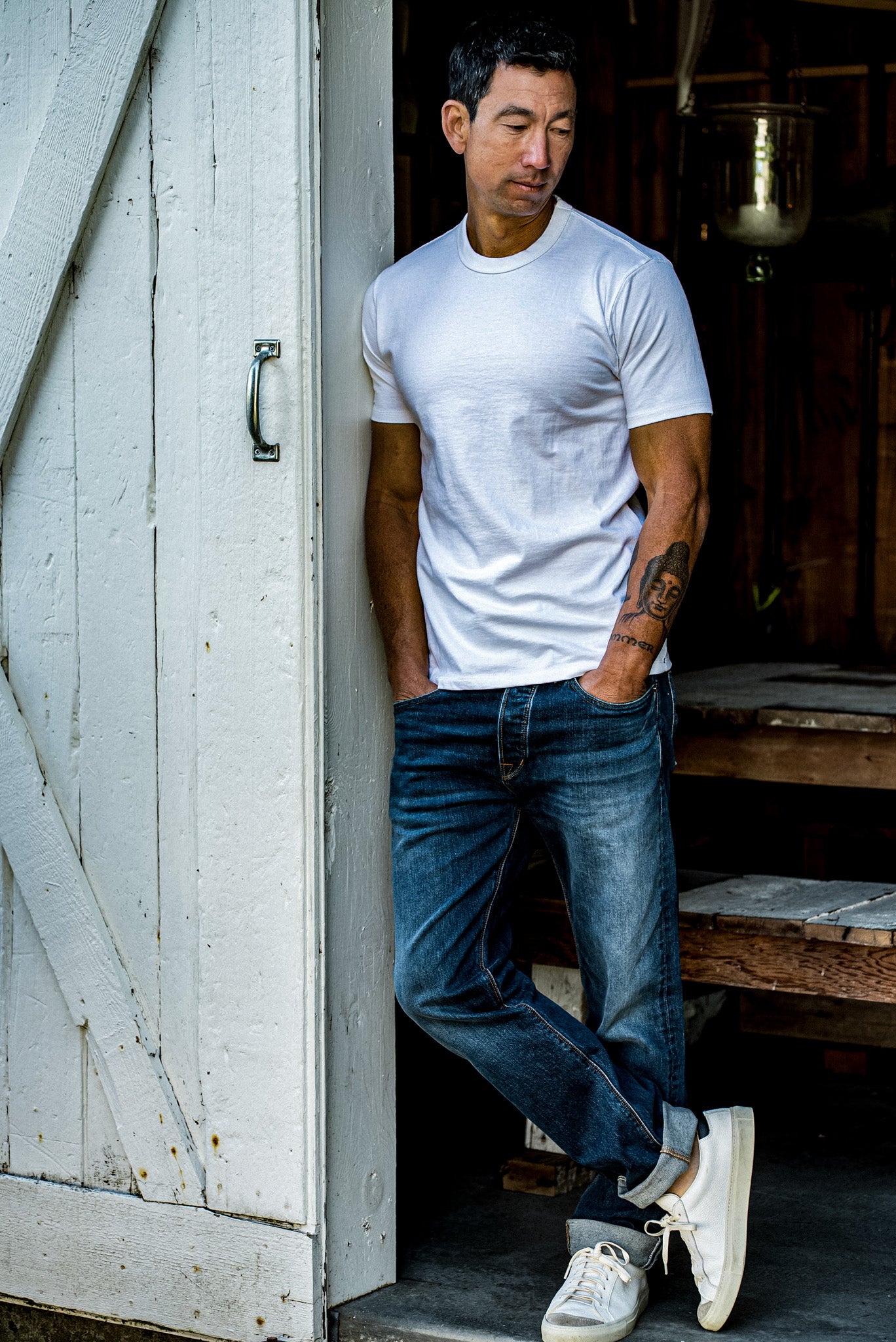 Man in white heavyweight Bolinas cotton tee leaning against a weathered barn door.