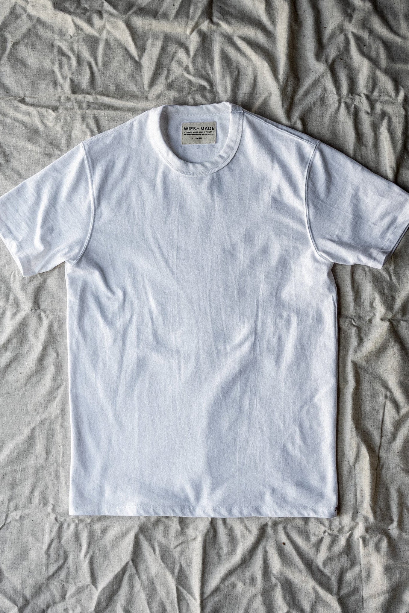 Bolinas heavyweight white cotton tee laid flat on linen, showing WiesMade Made in USA neck label.