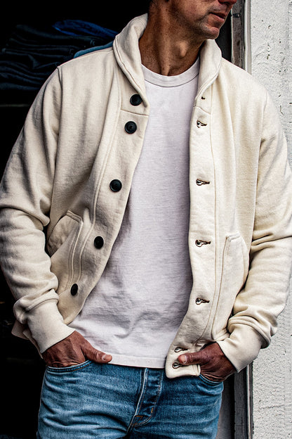 Man wearing a natural cream French terry shawl cardigan with black buttons over a white tee and jeans.