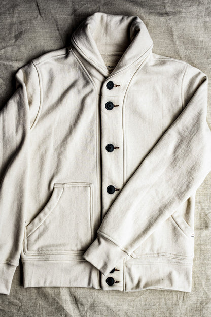 Natural cream shawl collar cardigan in cotton French terry with dark buttons, laid flat on linen.