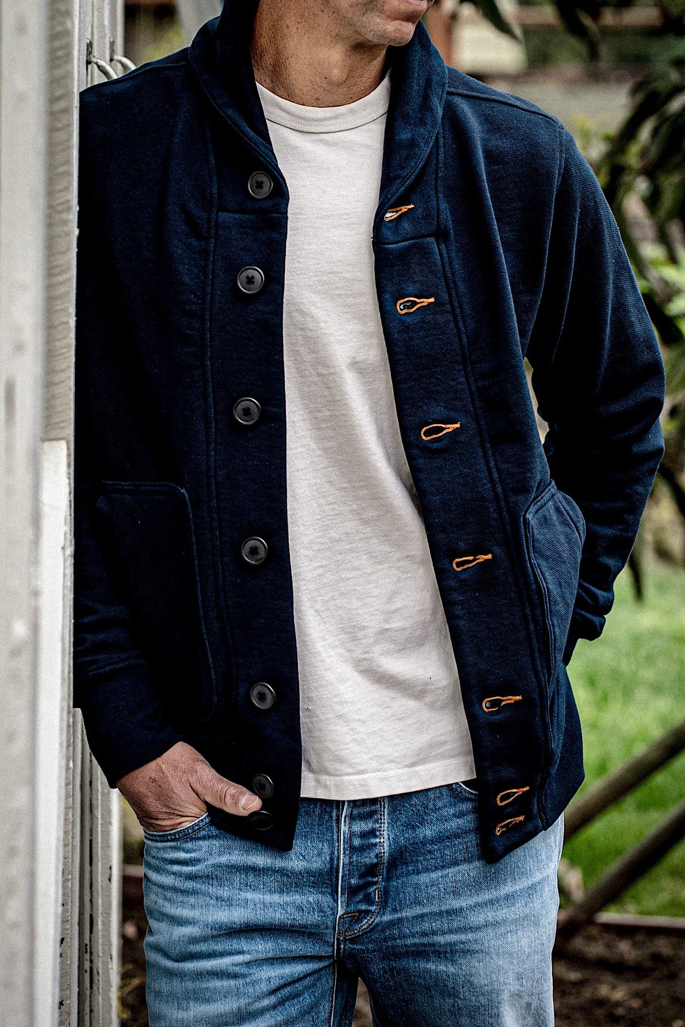 Navy French terry shawl cardigan with tobacco contrast keyholes, worn open over a cream tee and faded jeans.