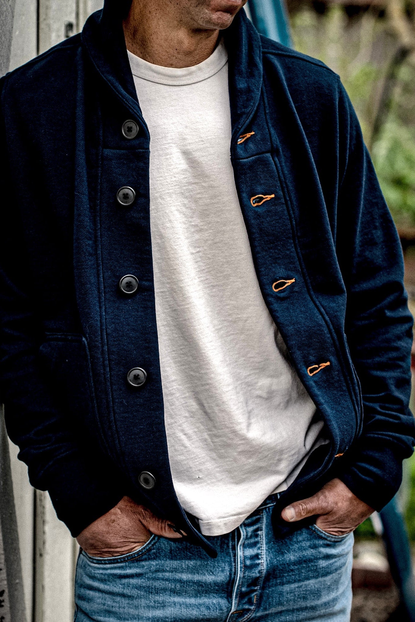 Navy French terry shawl cardigan worn open over a white tee with faded denim jeans, showing tobacco-thread contrast keyholes.
