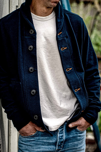Navy French terry shawl cardigan worn open over a white tee with faded denim jeans, showing tobacco-thread contrast keyholes.