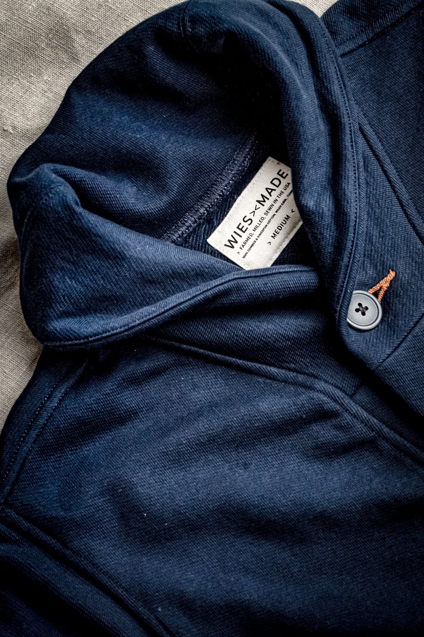 Close-up of navy French terry shawl cardigan showing grey button with tobacco thread keyhole and WiesMade label.
