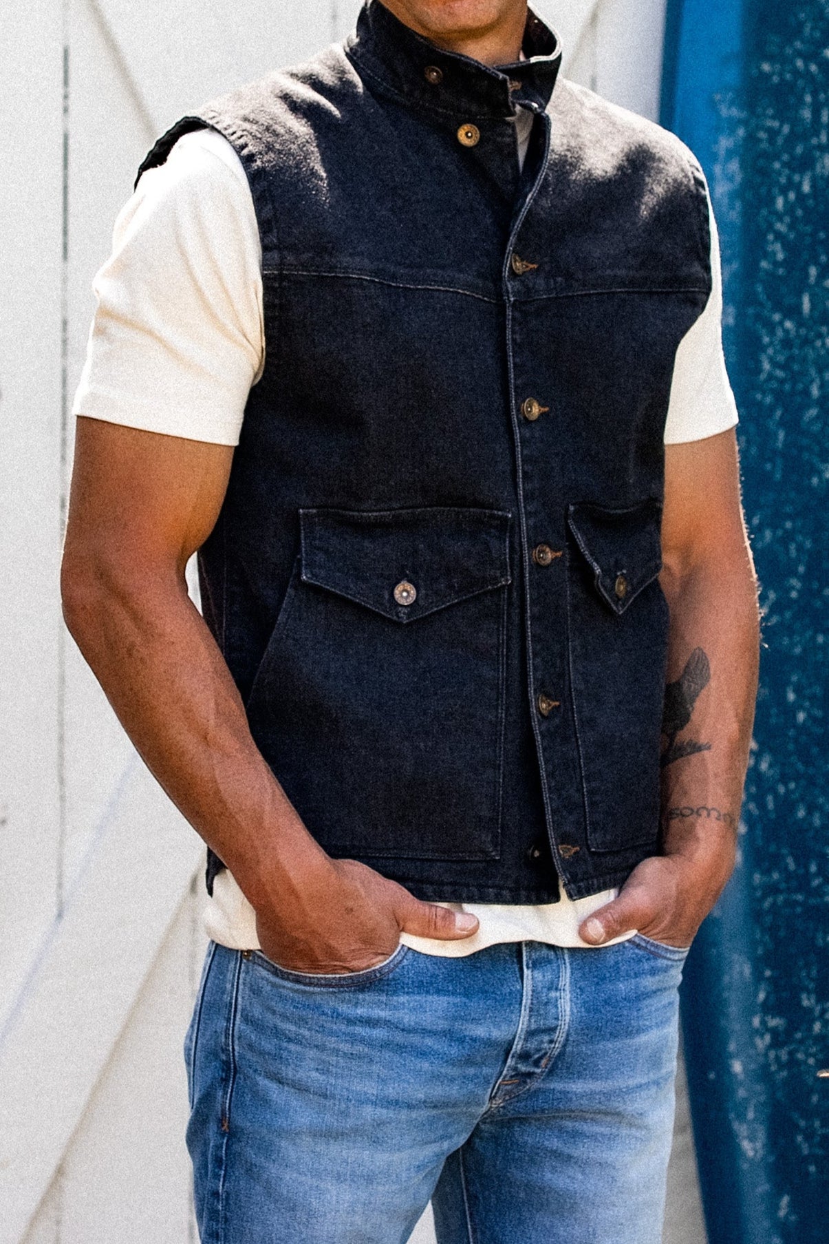 Black broken twill denim vest worn on-model with brass buttons and flap pockets.