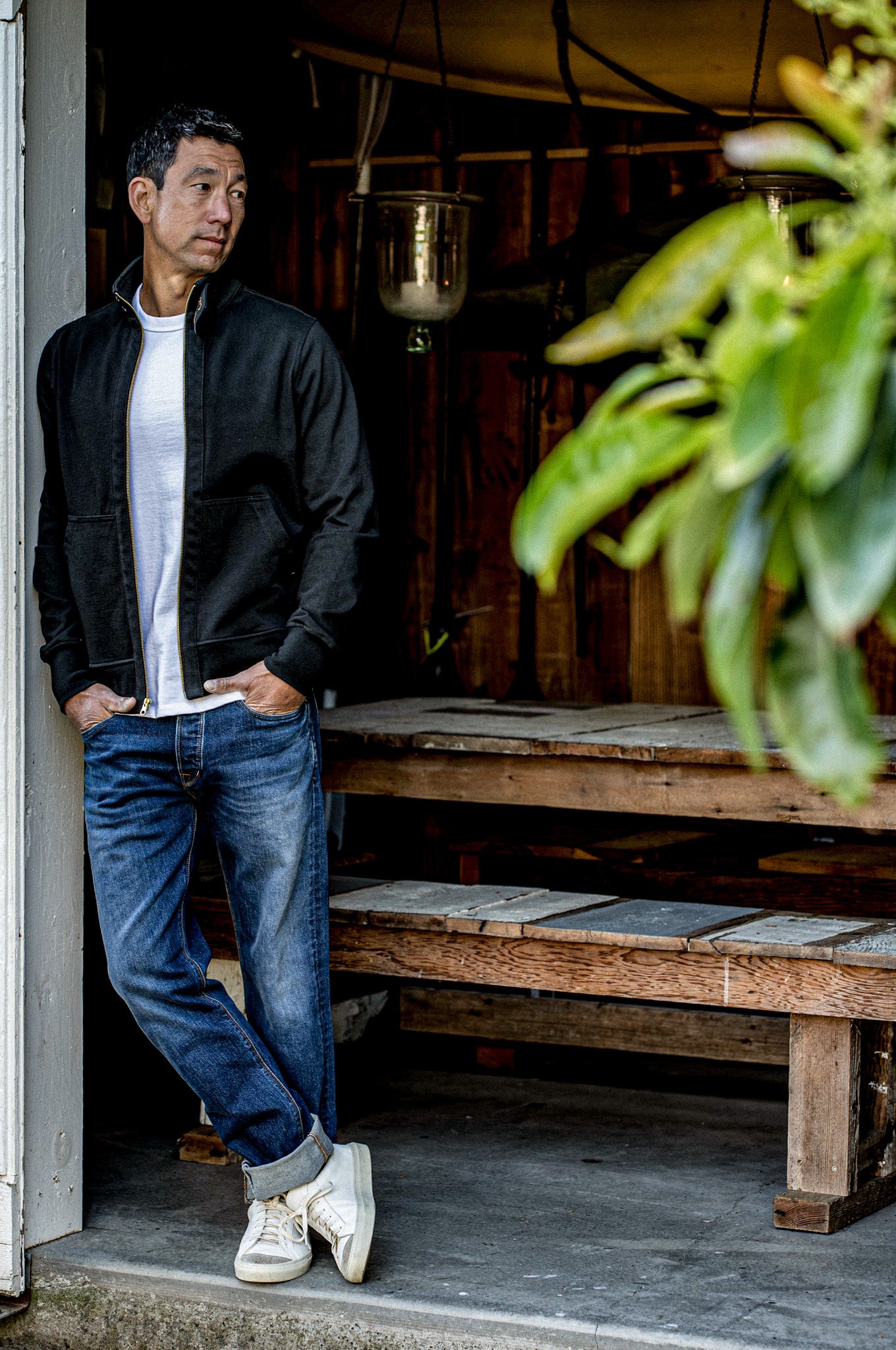 Man in a black Stinson cotton moto jacket with brass zipper, leaning in a doorway.