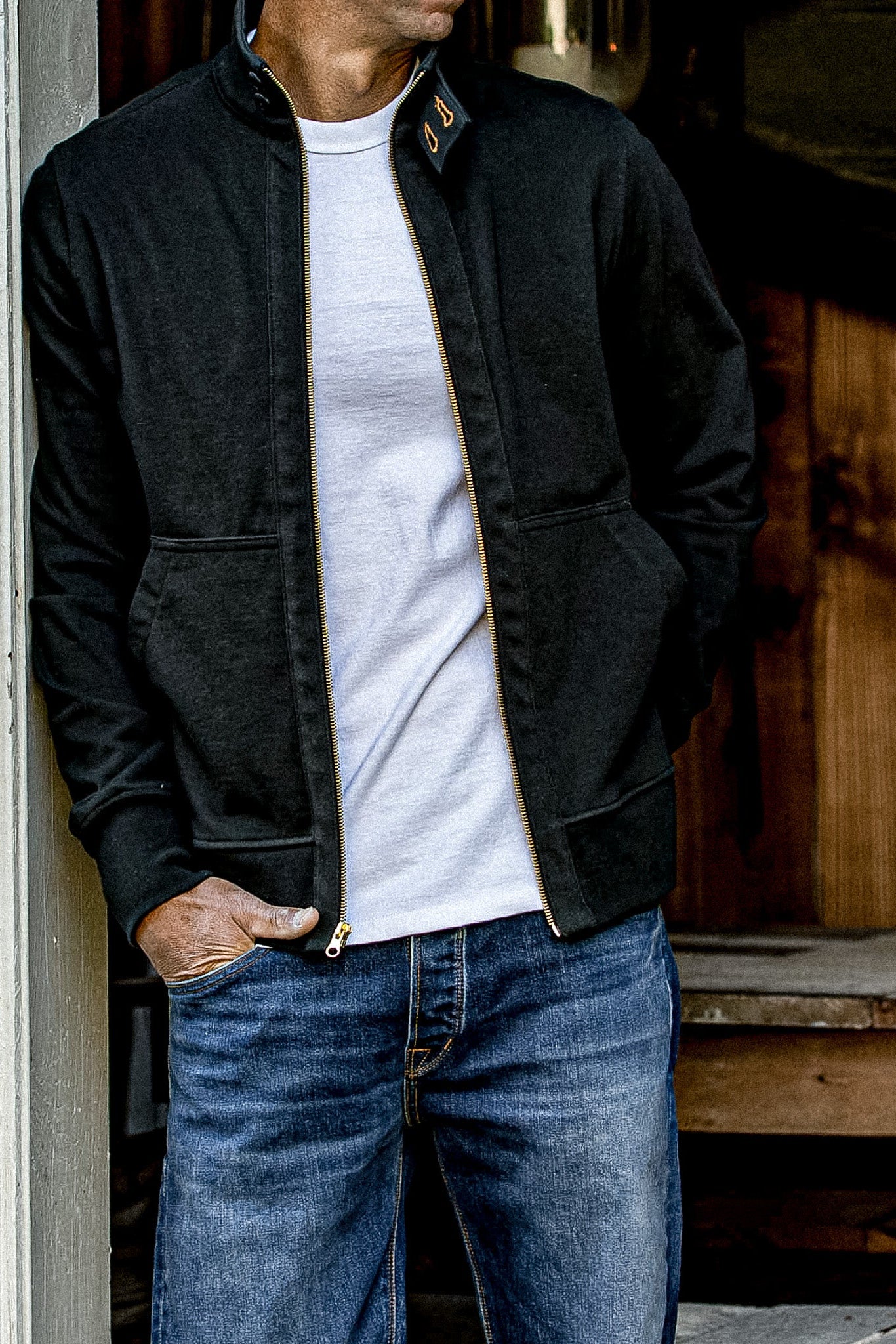 Man wearing an open black Stinson moto jacket with brass zipper over a white tee.