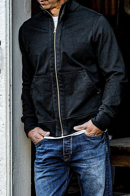 Man in a basalt cotton moto jacket with brass zipper worn over a white tee and jeans.