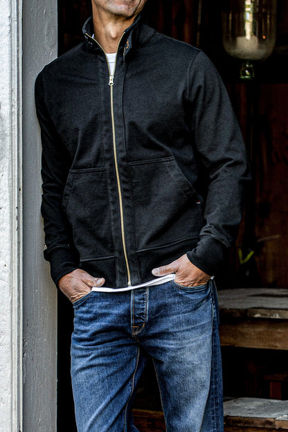 Man wearing a basalt cotton moto jacket with brass front zipper, hands in jean pockets.