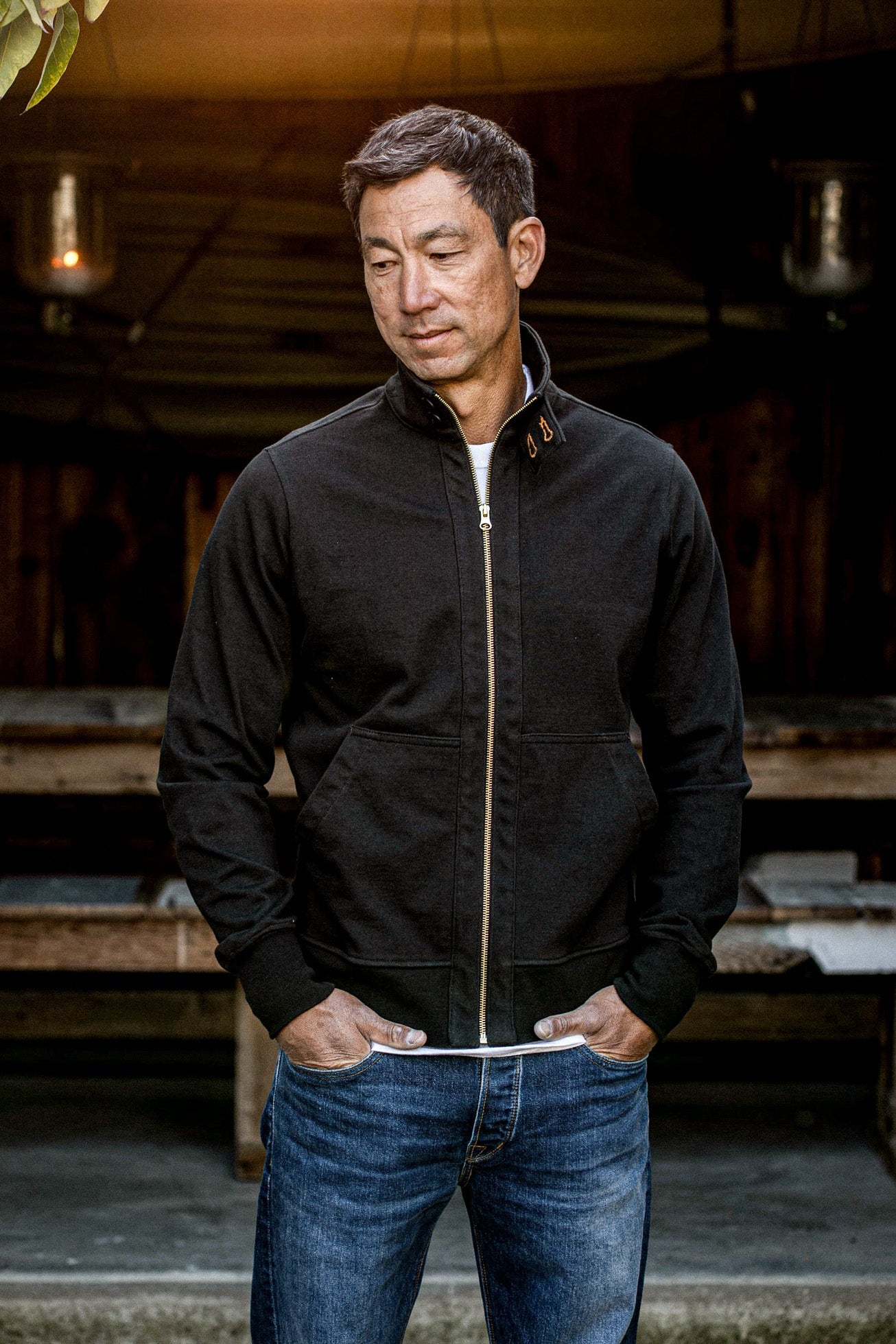 Man wearing a basalt black cotton Stinson moto jacket with brass zipper, worn open over jeans.
