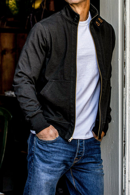 Man wearing an open black cotton Stinson moto jacket with brass zipper over jeans.