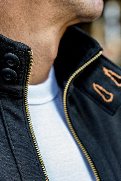 Brass zipper and black buttons detailing a men's cotton moto jacket worn over a white tee.