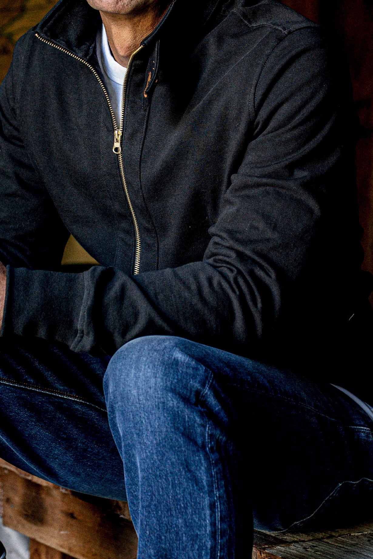 Man wearing black Stinson Moto cotton jacket with brass zipper, styled over blue jeans.