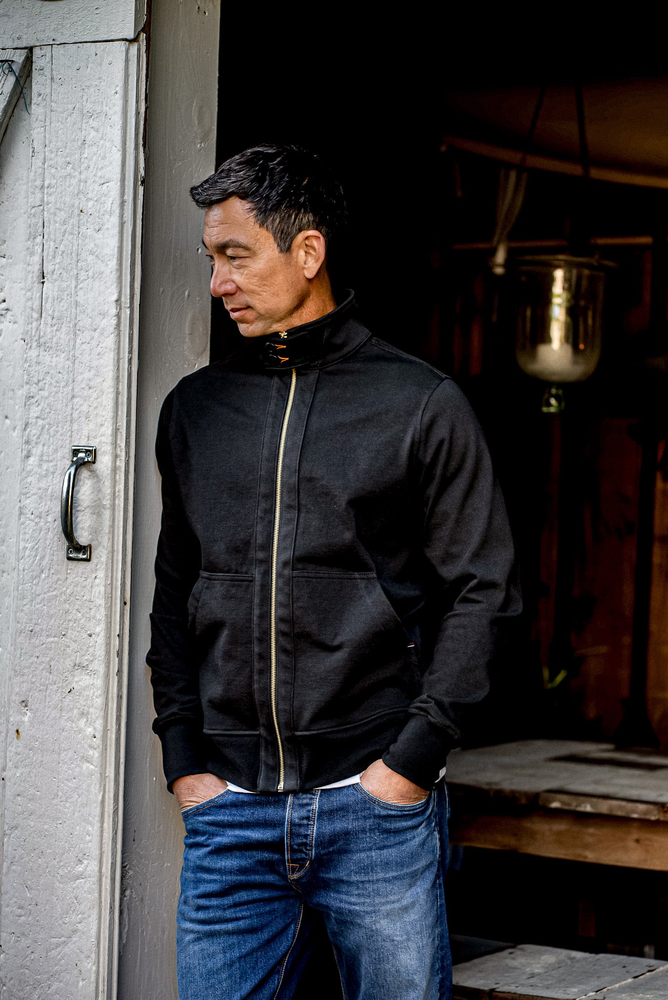 Man wearing a black Stinson Moto jacket with brass zipper, hands tucked into jeans pockets.