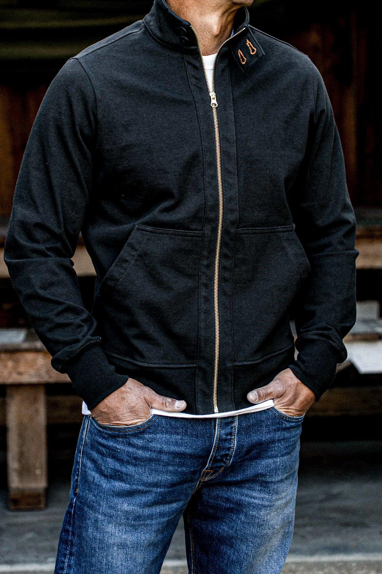 Man wearing a black cotton moto jacket with brass zipper over blue jeans.