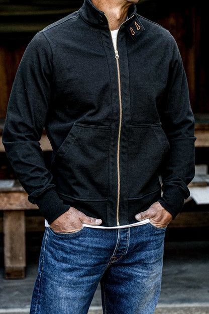 Man wearing a black cotton moto jacket with brass zipper over blue jeans.