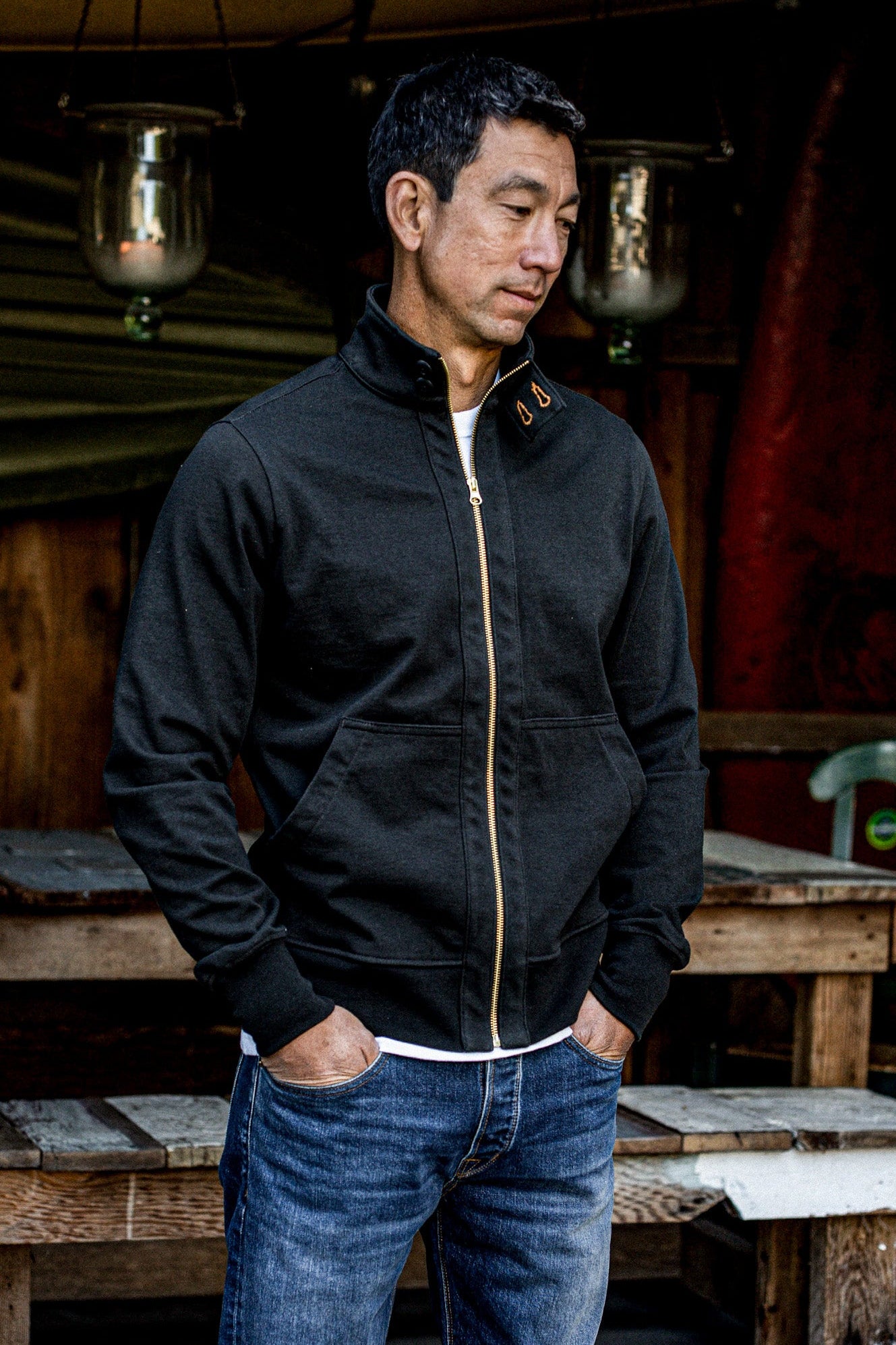 Man wearing black cotton moto jacket with brass zipper, layered over jeans outdoors.