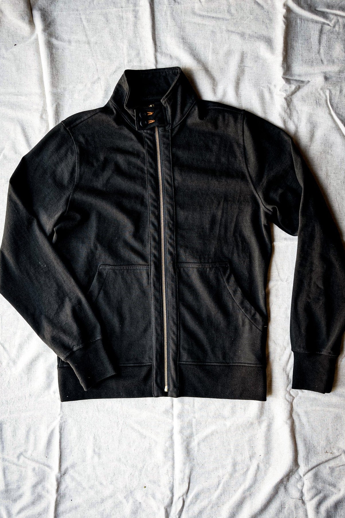 Basalt black cotton moto jacket laid flat with stand collar and brass front zipper.