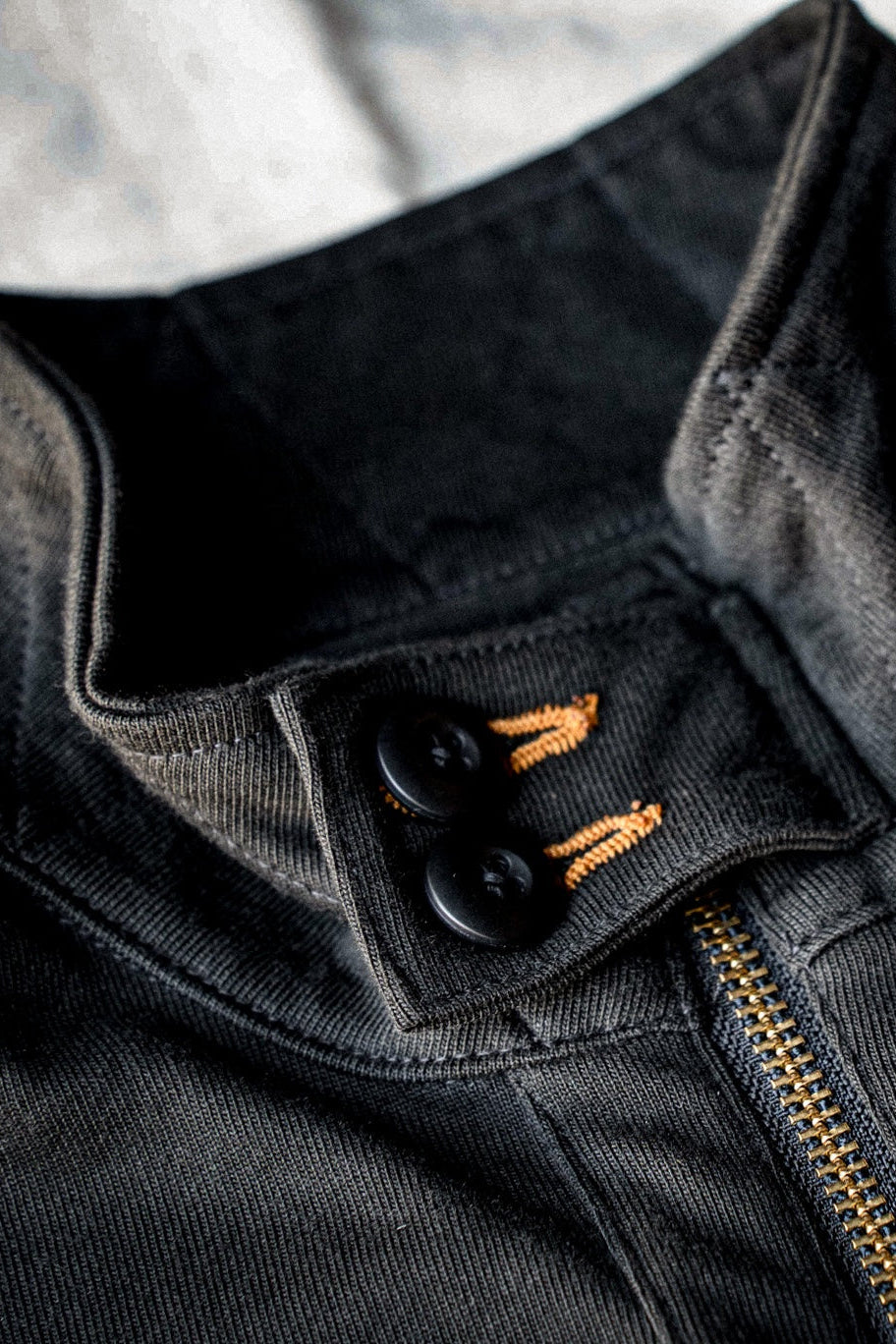 Close-up of black buttons with orange keyhole stitching and brass zipper on a basalt cotton moto jacket.