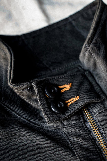 Close-up of black buttons with orange keyhole stitching and brass zipper on a basalt cotton moto jacket.