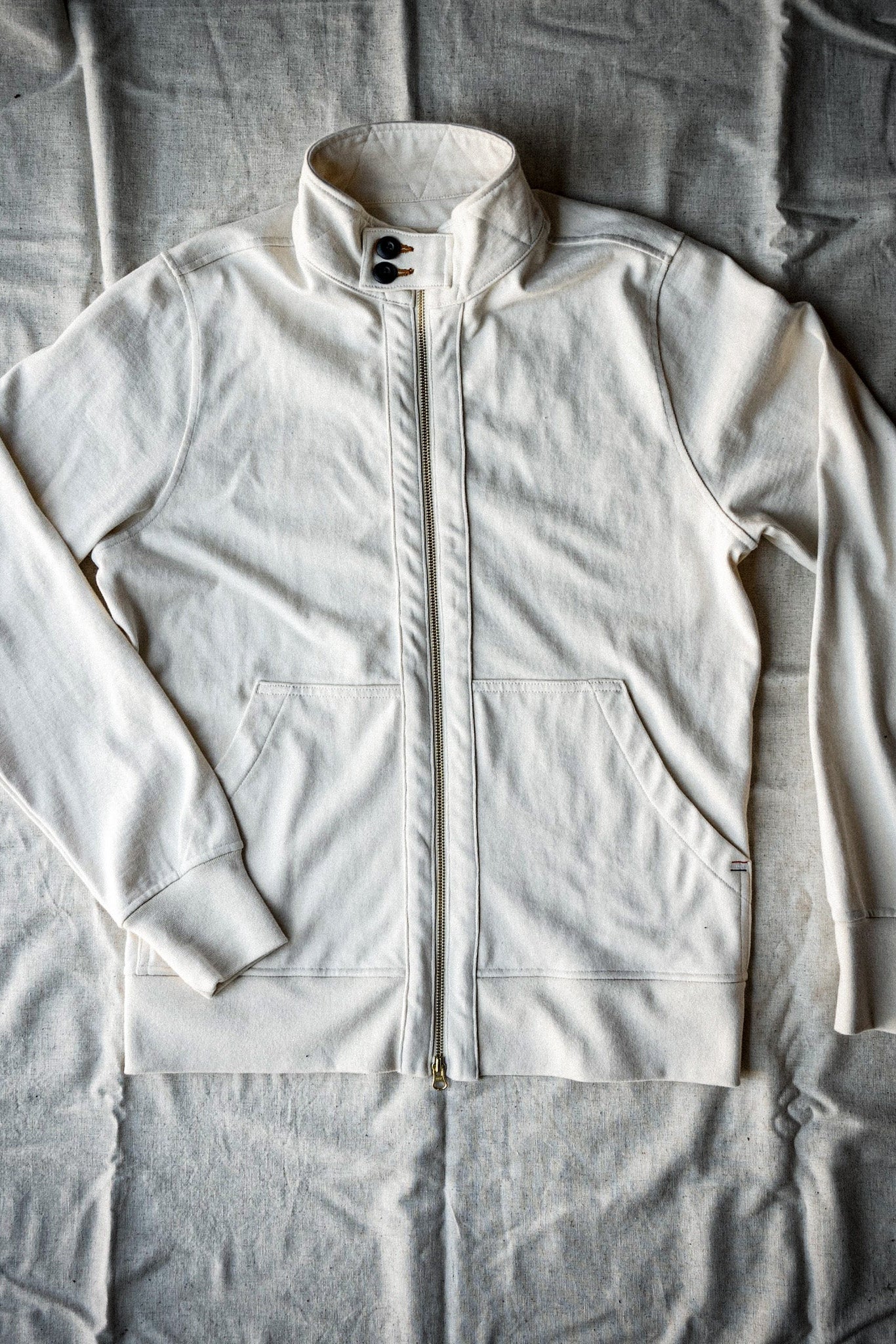 Natural cotton Stinson moto zip jacket laid flat, brass front zipper and stand collar.