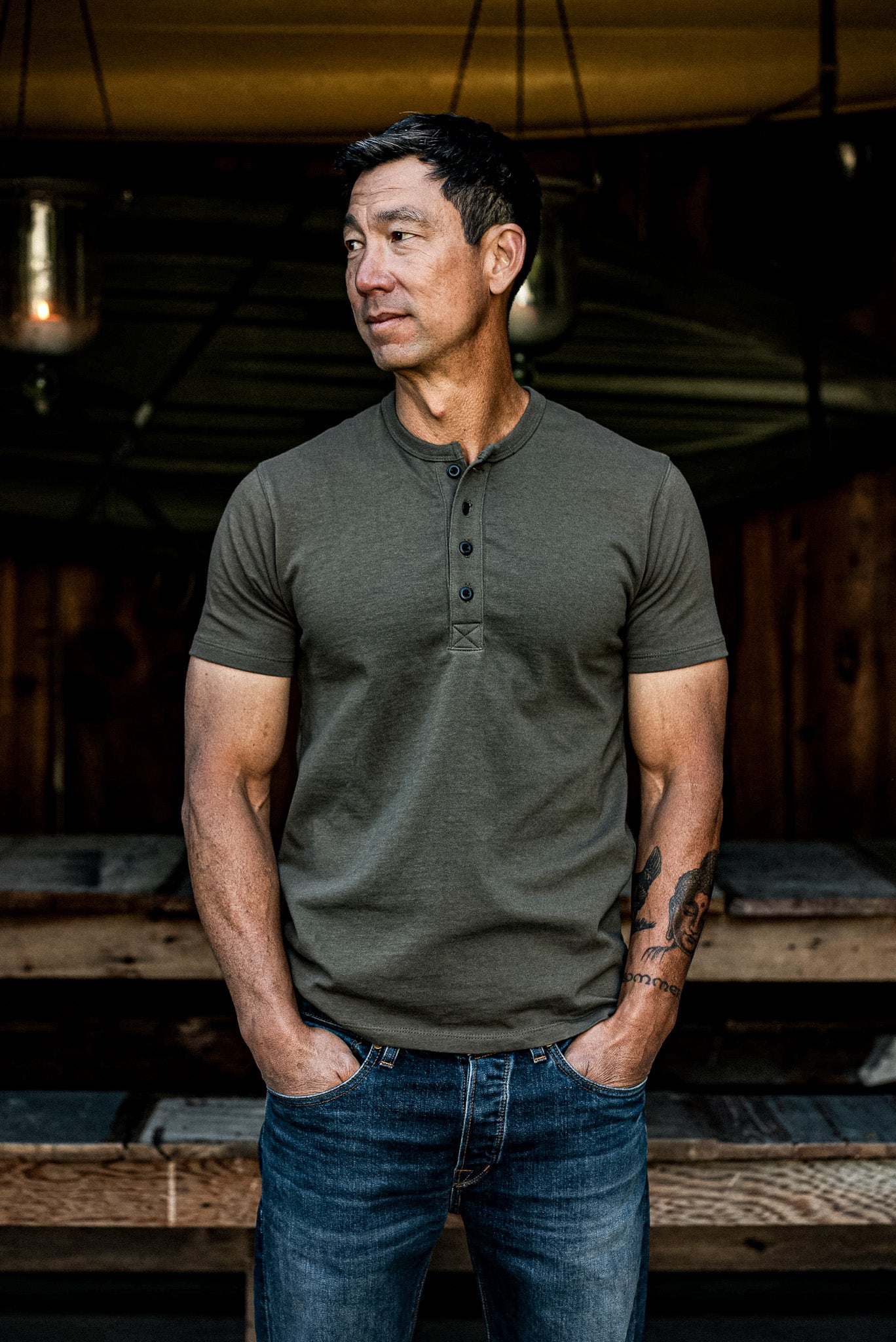Man wearing an olive short-sleeve Bolinas Henley with four-button placket, paired with blue jeans.
