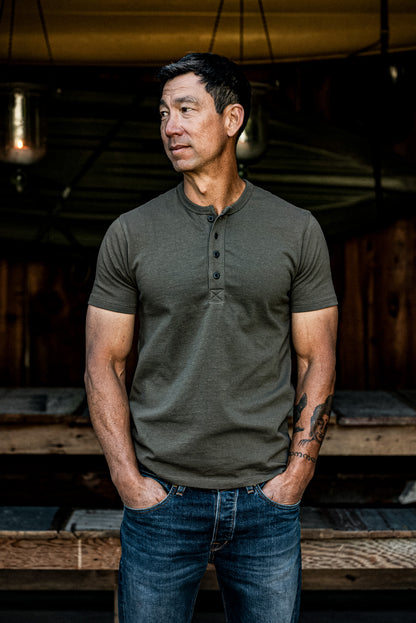 Man wearing an olive short-sleeve Bolinas Henley with four-button placket, paired with blue jeans.