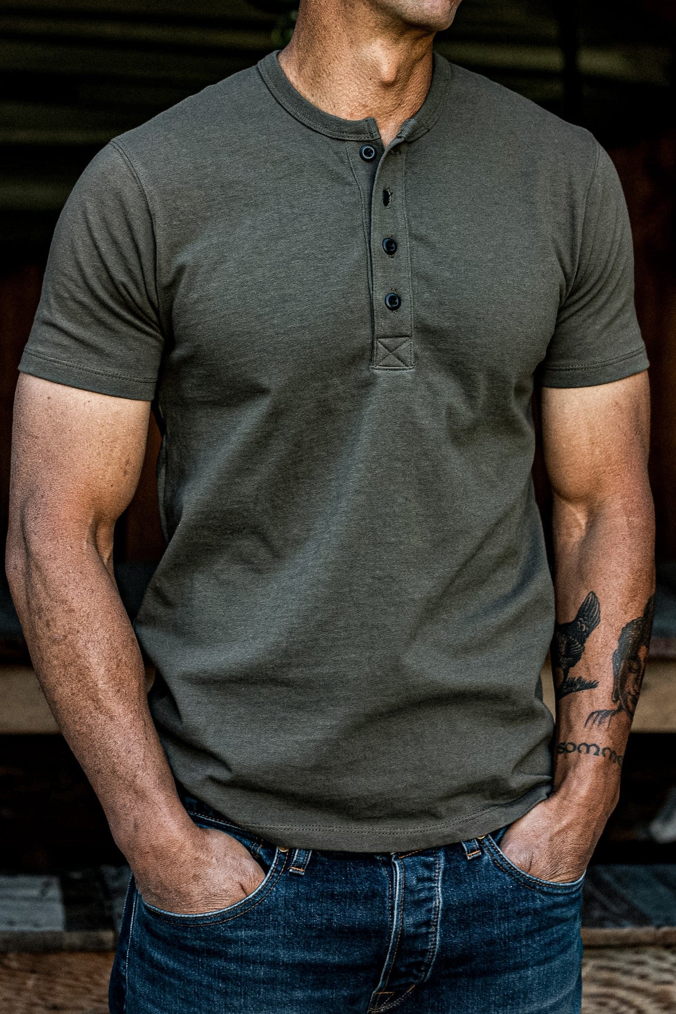Man wearing the olive Bolinas four-button Henley short-sleeve shirt with dark denim jeans.