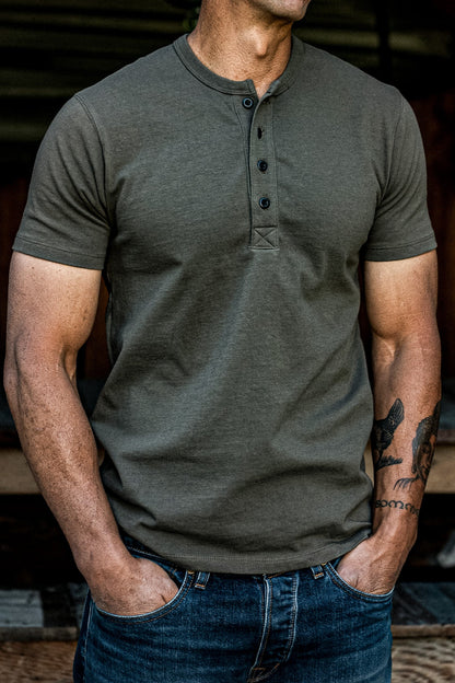 Man wearing the olive Bolinas four-button Henley short-sleeve shirt with dark denim jeans.