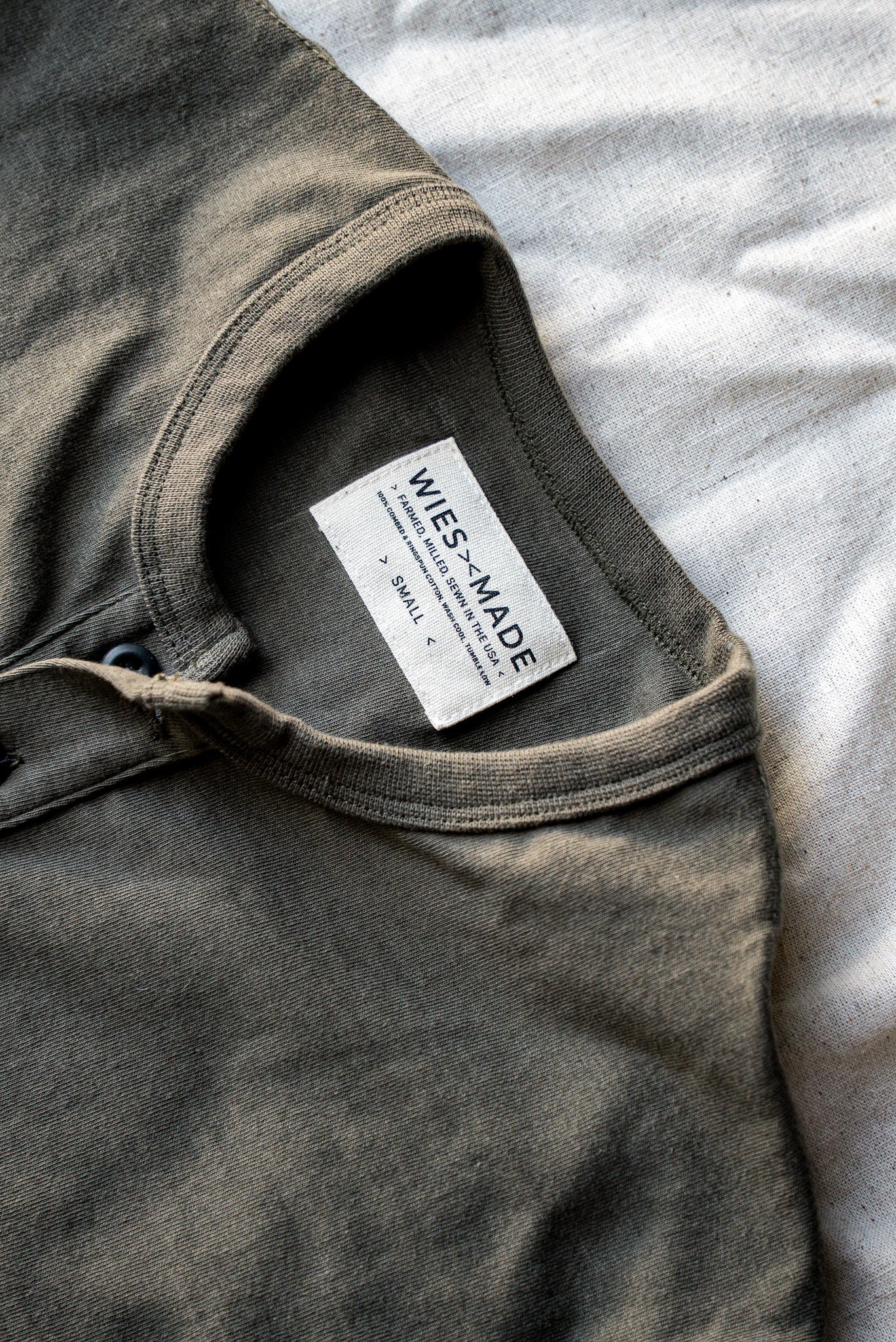 Close-up of olive Bolinas Henley collar and button placket with WiesMade interior tag noting cotton made in the USA.