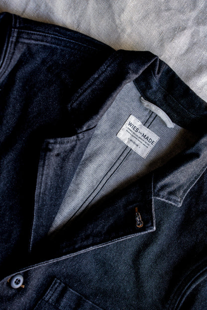 Close-up of black denim chore blazer showing WiesMade interior label, lapel stitching, and button.