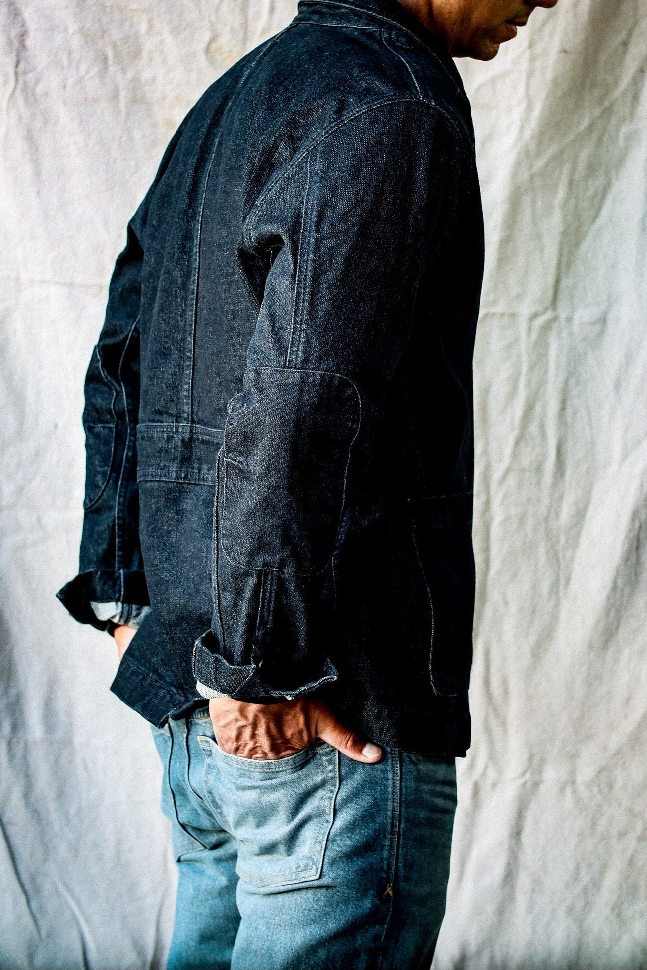 Side view of the men's denim blazer in dark indigo, showing the double-layered elbow patch and side pocket.